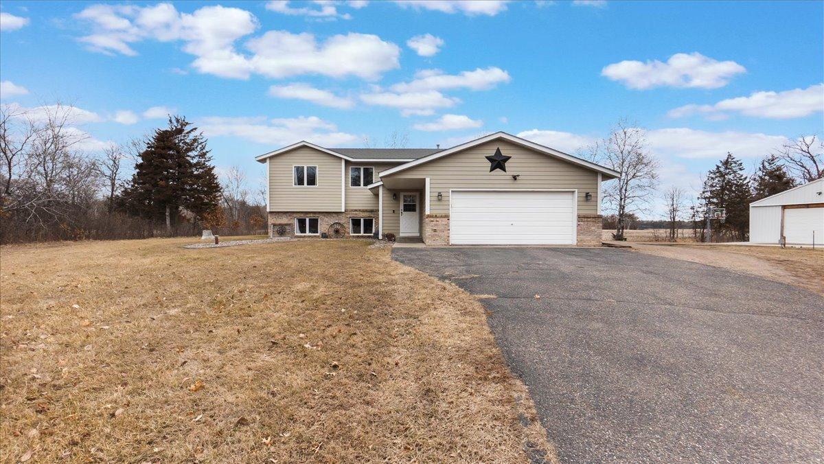 Beige split-level home with brick accents, a two-car garage, and a detached outbuilding.