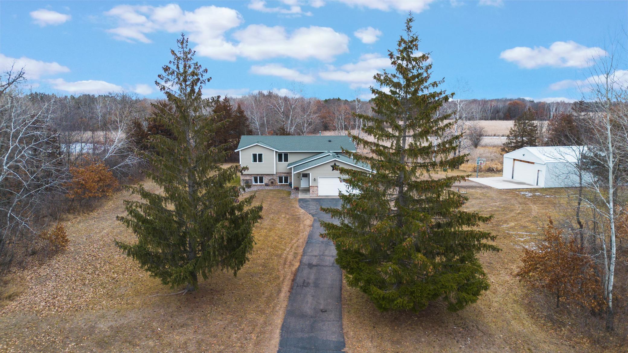 Aerial view of a home with a long driveway, large detached outbuilding, and wooded grounds.