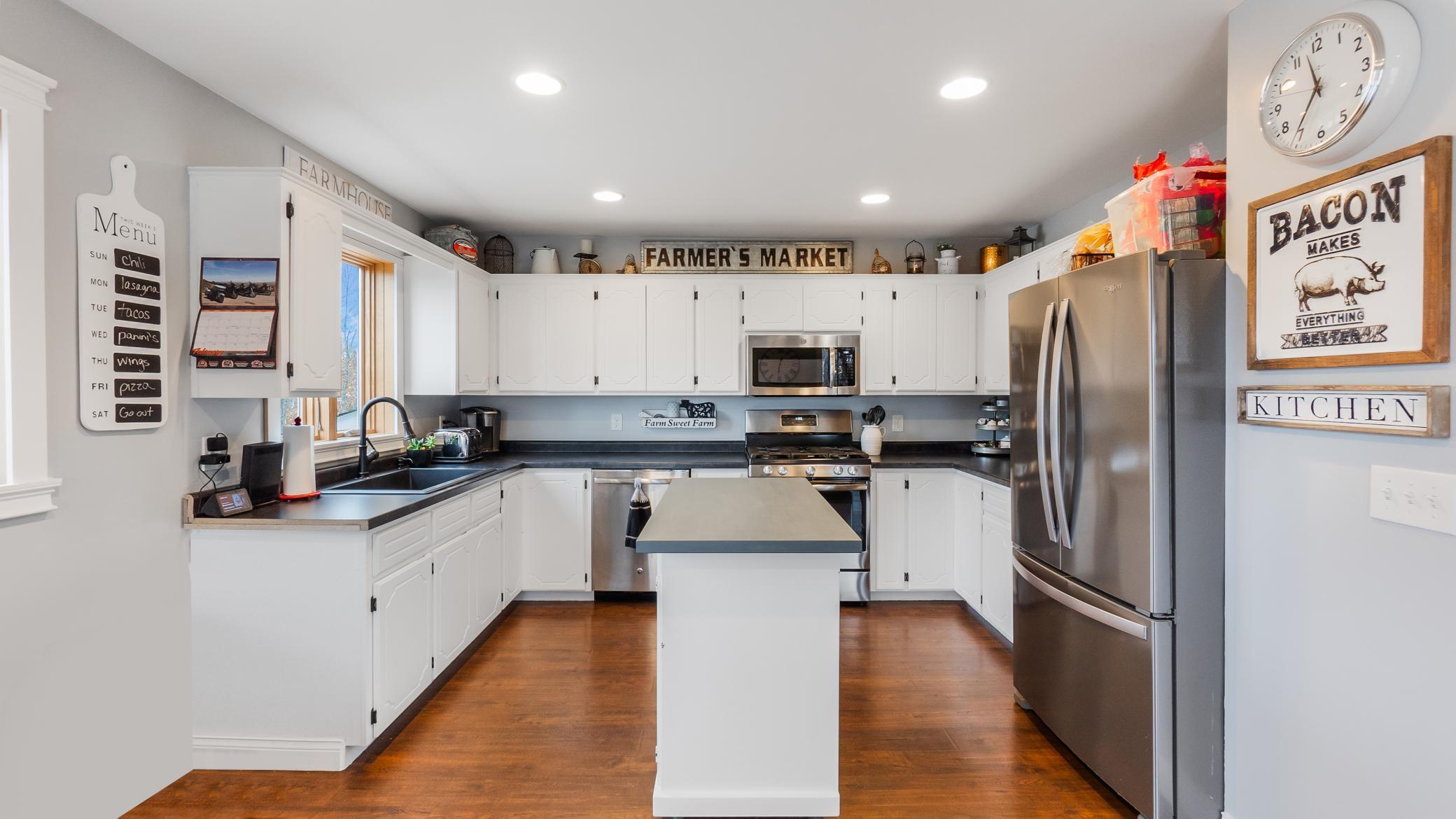 Farmhouse kitchen with white cabinets, central island, stainless steel appliances, and warm wood floors.
