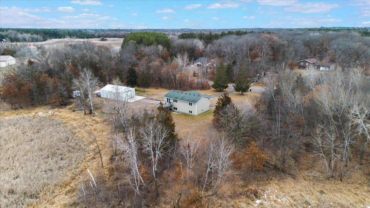 Aerial view of a home and white outbuilding amid open land and mature woodland.