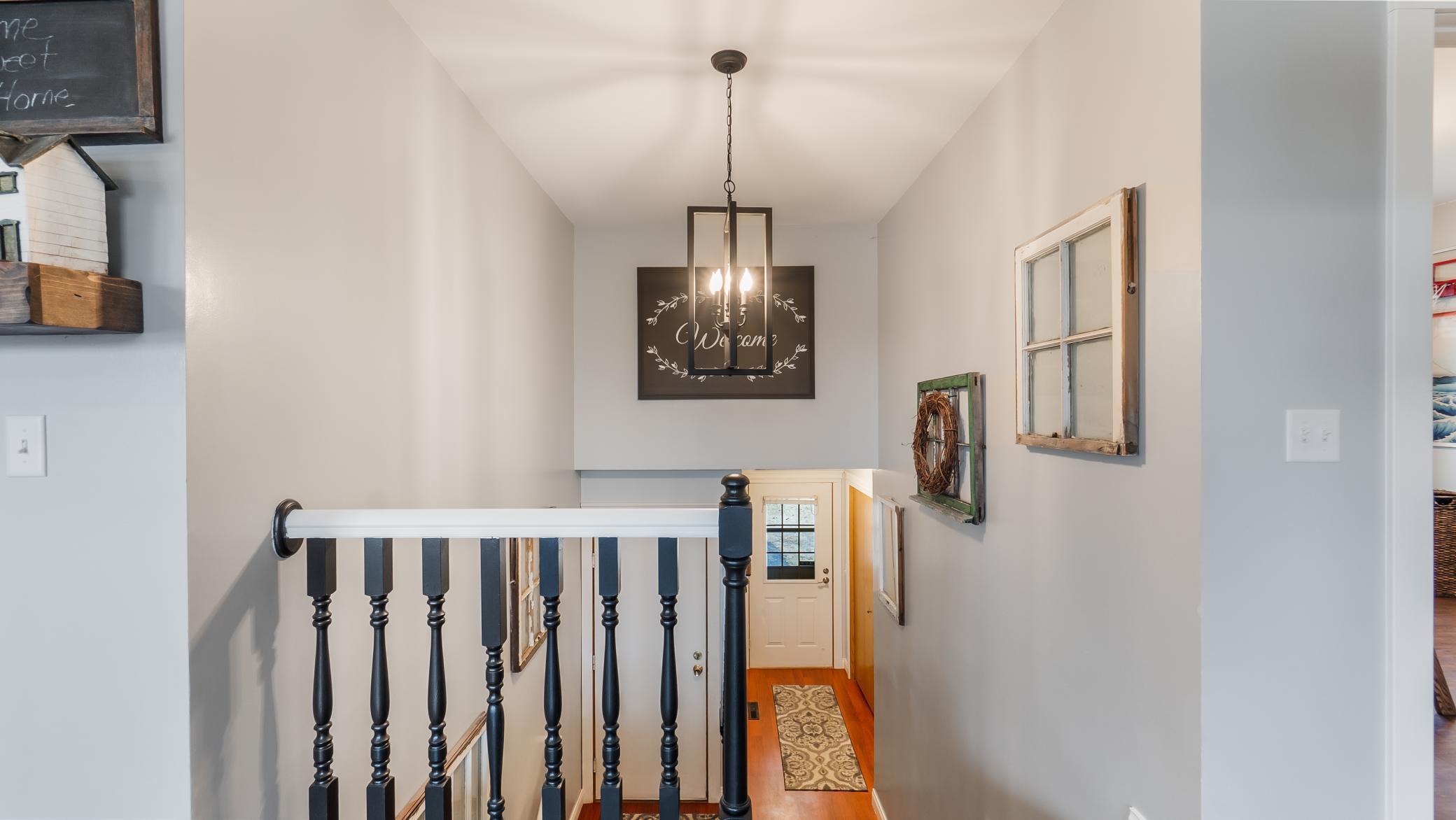 Upstairs landing with a black-and-white railing, hardwood hallway, and hanging chandelier.