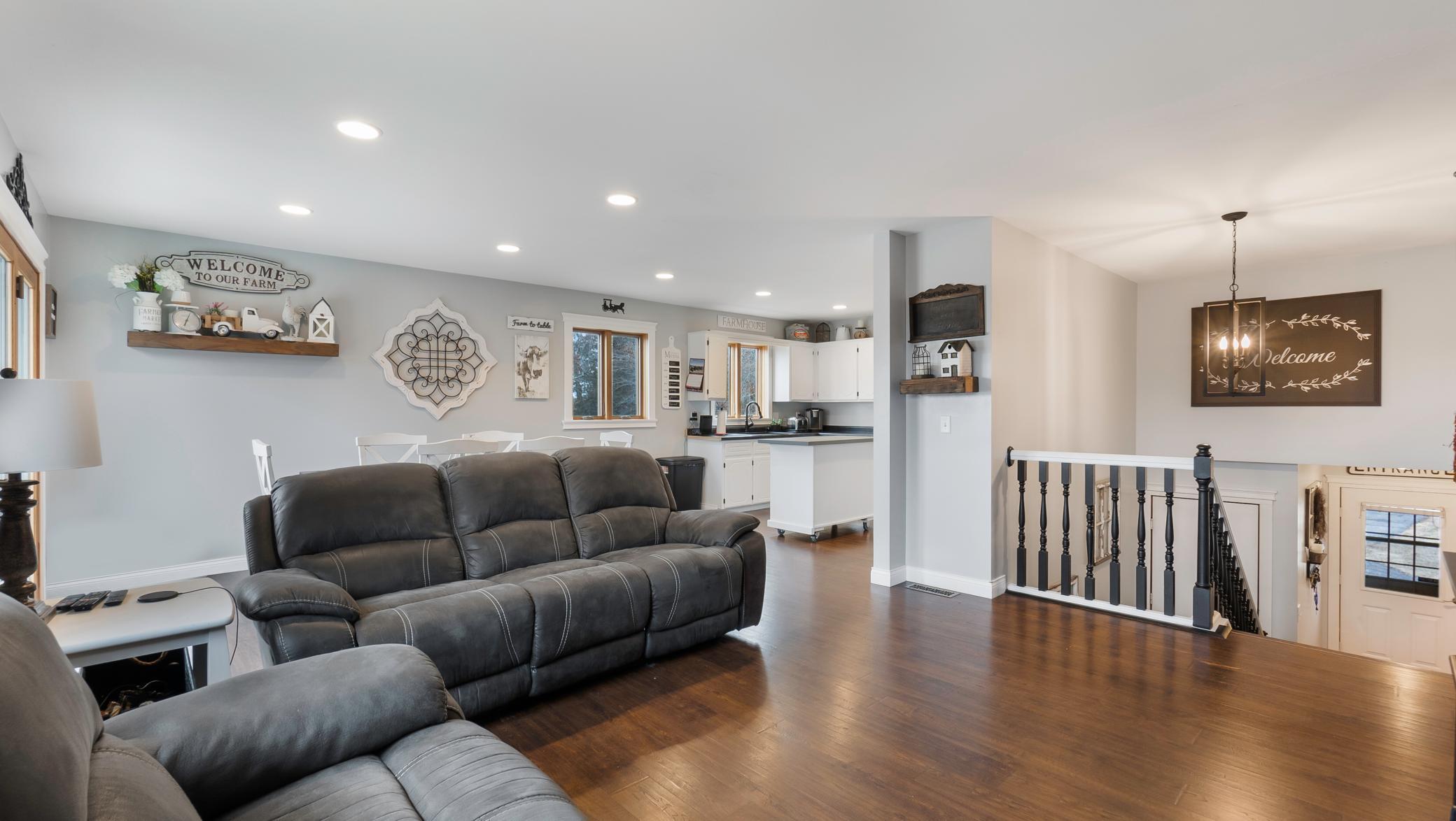 Open-plan living room and kitchen with leather sofas, hardwood floors, and farmhouse decor.