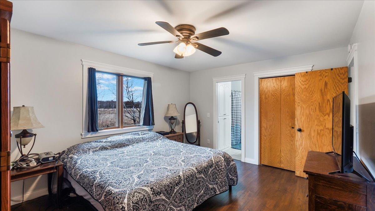 Bedroom with a patterned bedspread, dark wood floors, and a window overlooking an open field.