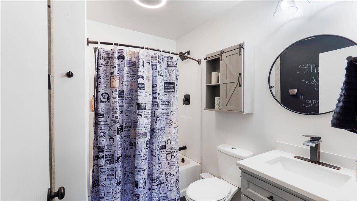 Bathroom with a newspaper-print shower curtain, gray vanity, and round mirror.