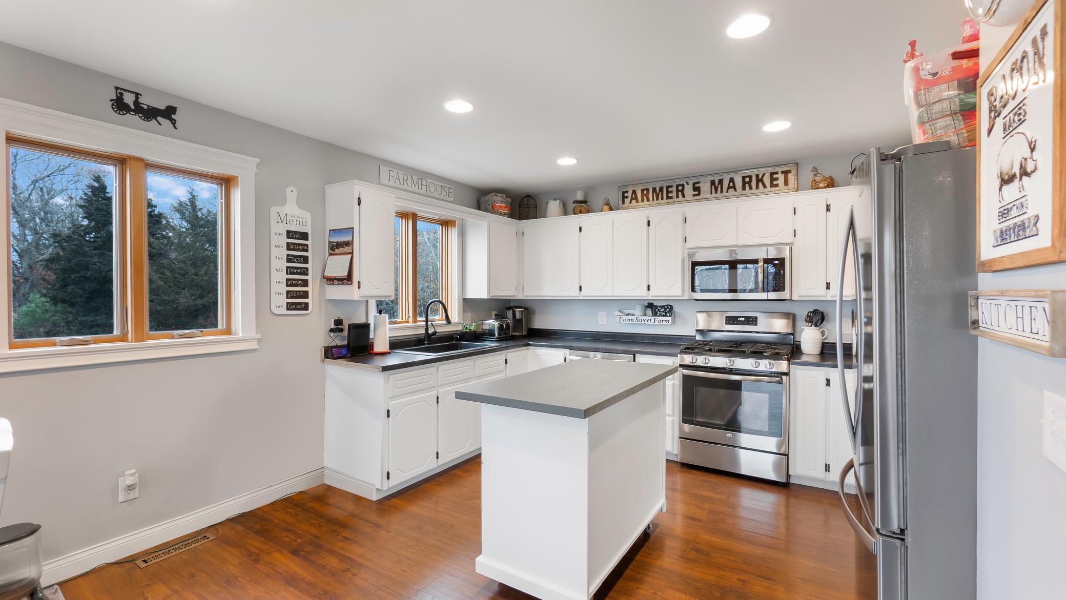 Farmhouse kitchen with white cabinets, a central island, stainless steel appliances, and wood-trimmed windows.