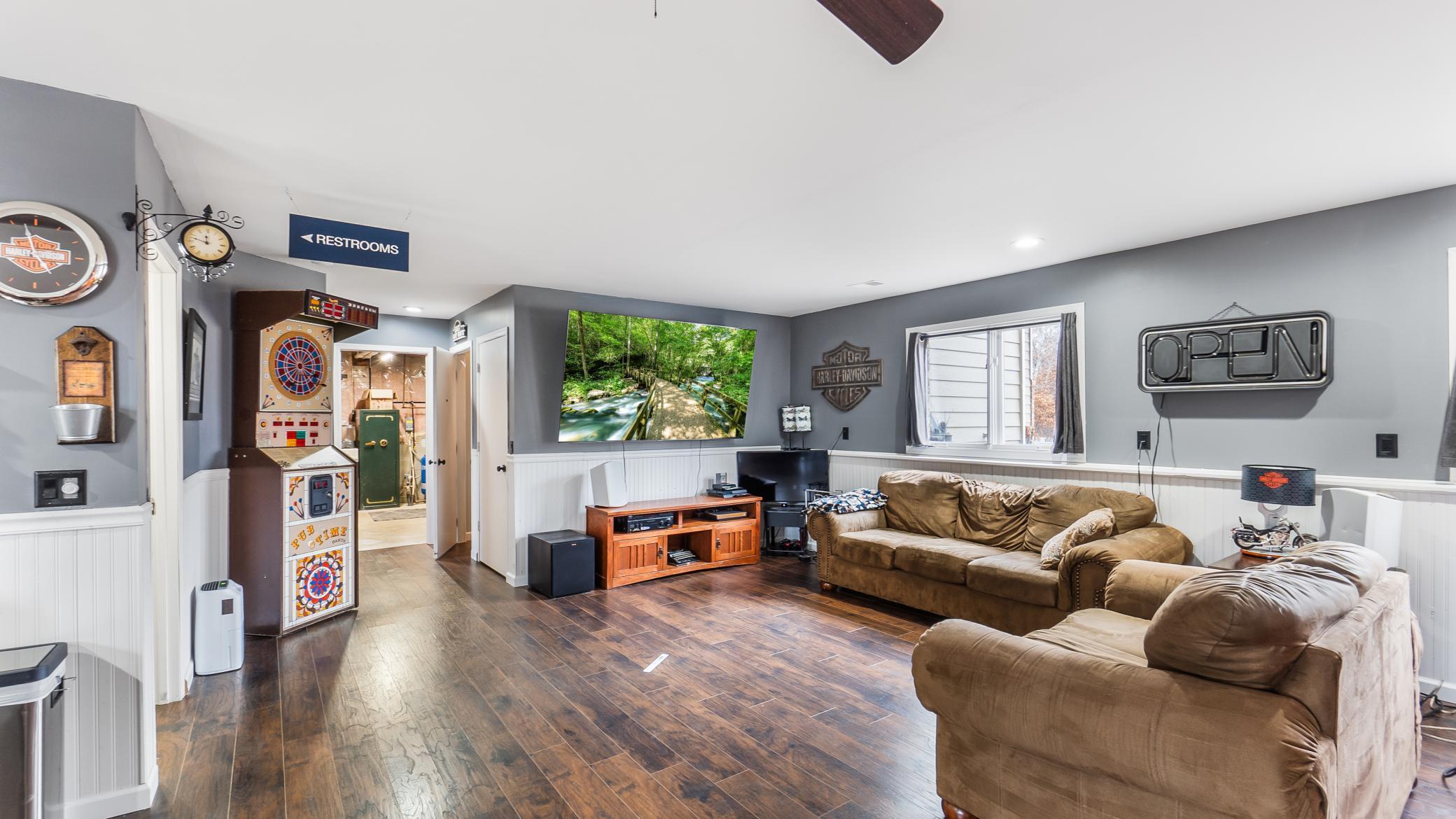 Furnished recreation room with brown leather sofas, a colorful pinball machine, and Harley-Davidson decor.