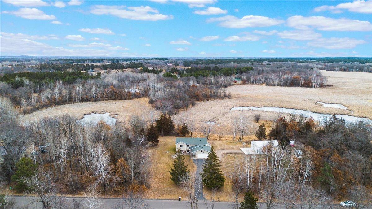 Aerial view of a rural home and outbuilding beside wooded marshland.