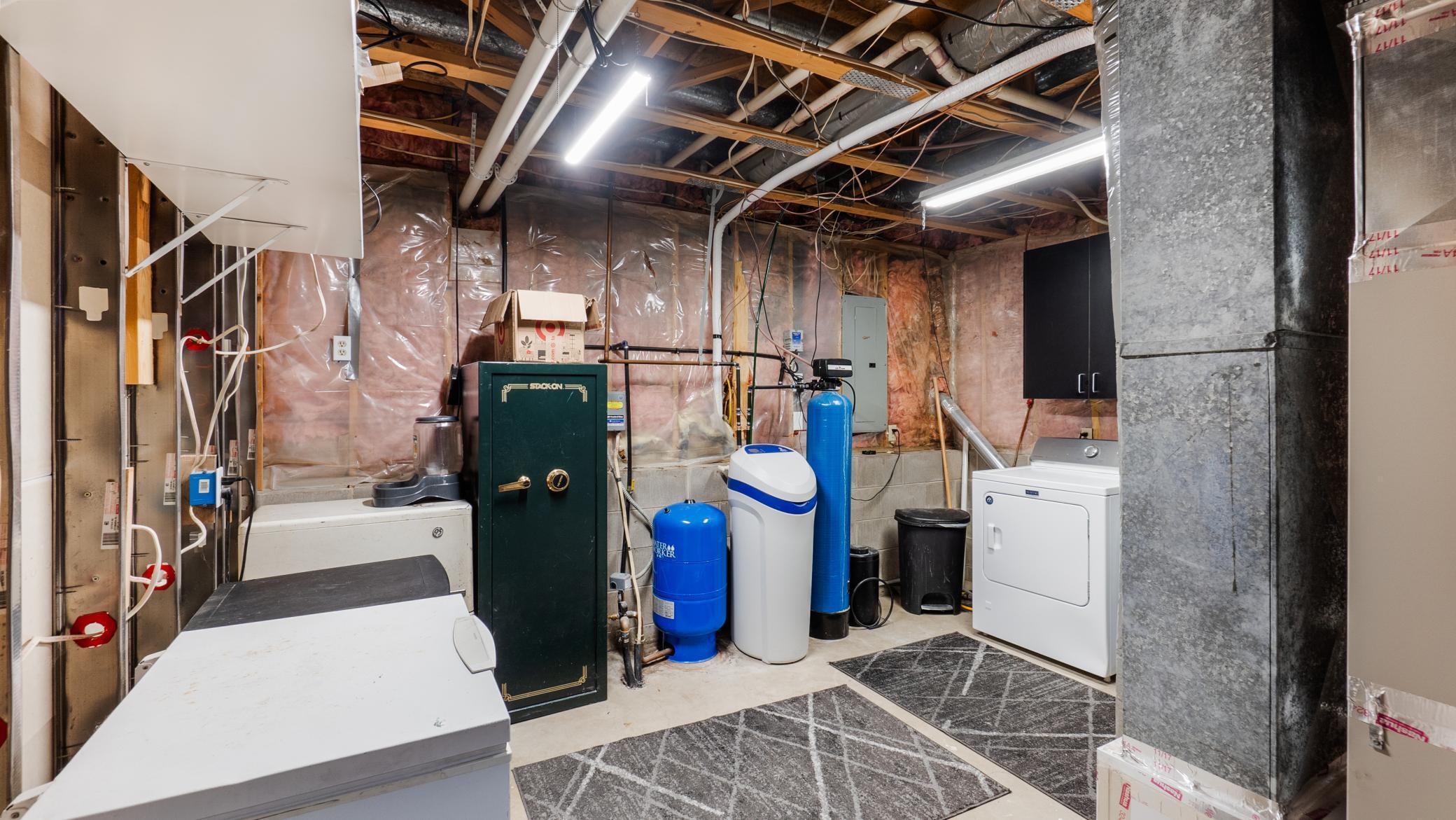 Basement utility room with laundry appliances, water treatment equipment, exposed insulation, and a green safe.