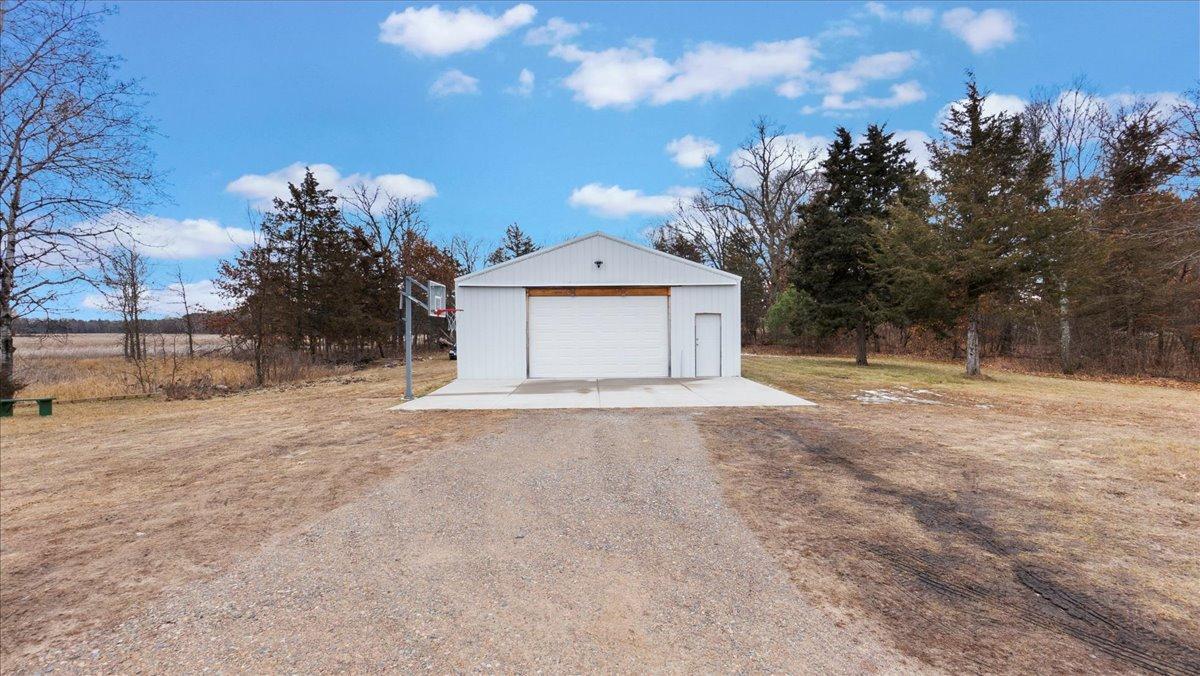 White detached garage with a gravel driveway, concrete apron, and basketball hoop beside it.