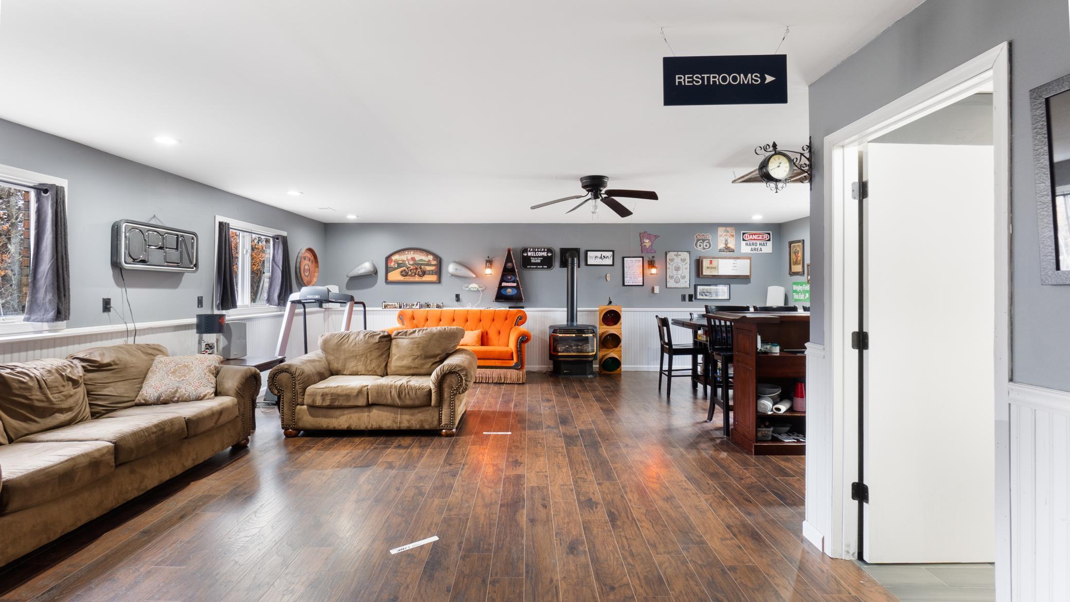 Furnished recreation room with brown sofas, an orange settee, wood-look flooring, and a bar counter.