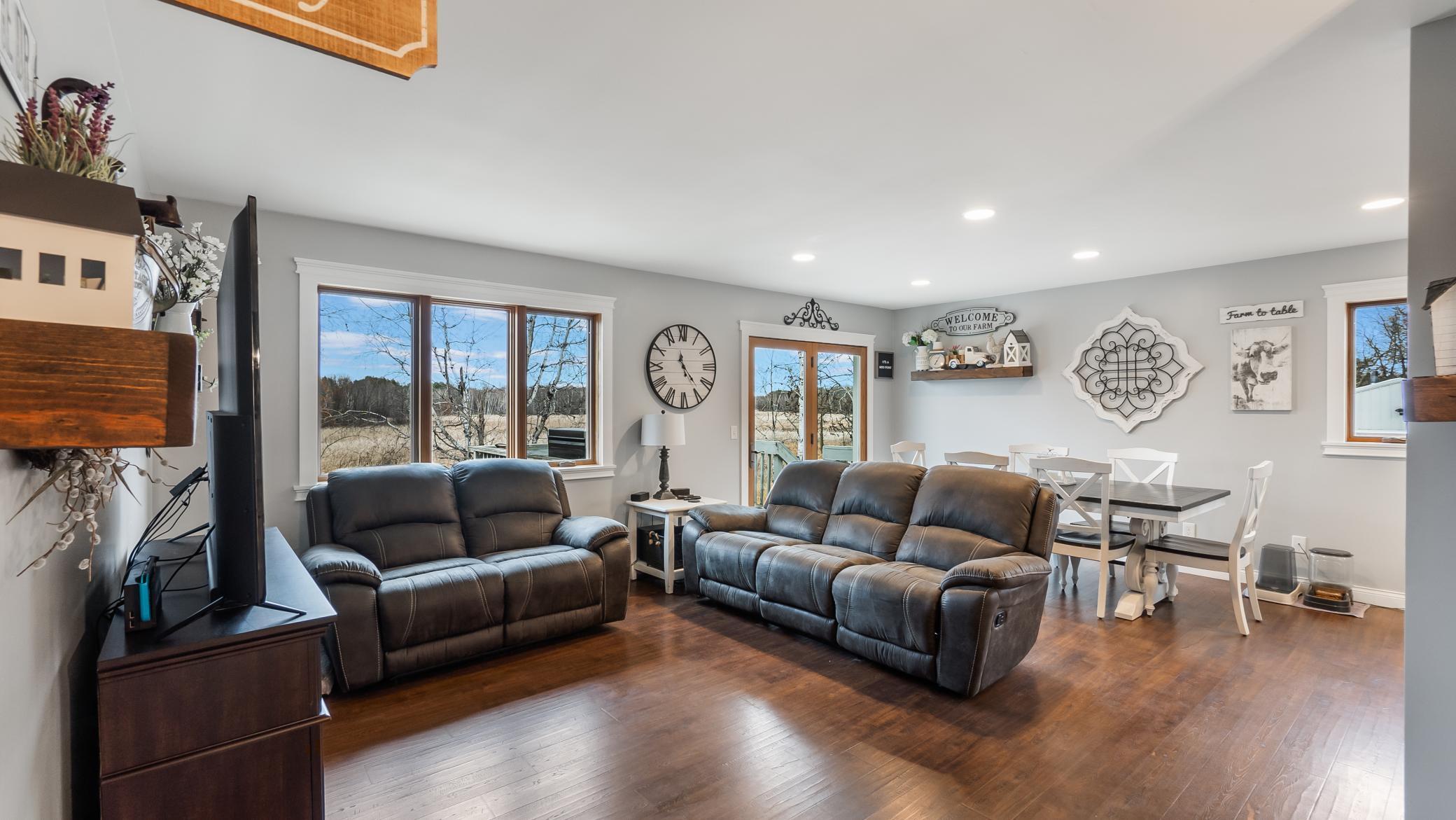 Open-plan living and dining room with leather sofas, hardwood floors, and large yard-facing windows.