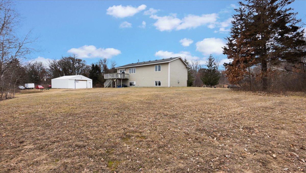 Beige two-story home with a raised deck and detached garage beyond a broad leaf-covered lawn.