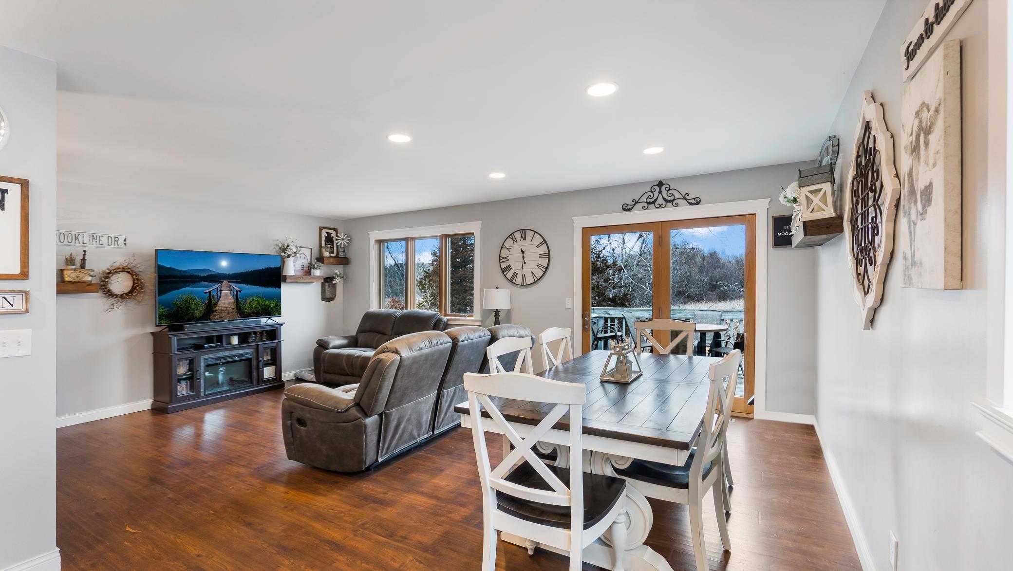 Open-plan living and dining room with gray recliners, a white dining set, and sliding doors facing snowy trees.
