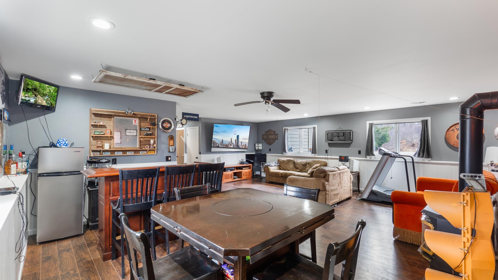 Furnished basement recreation room with a large game table, sofa, treadmill, and arcade-style games.