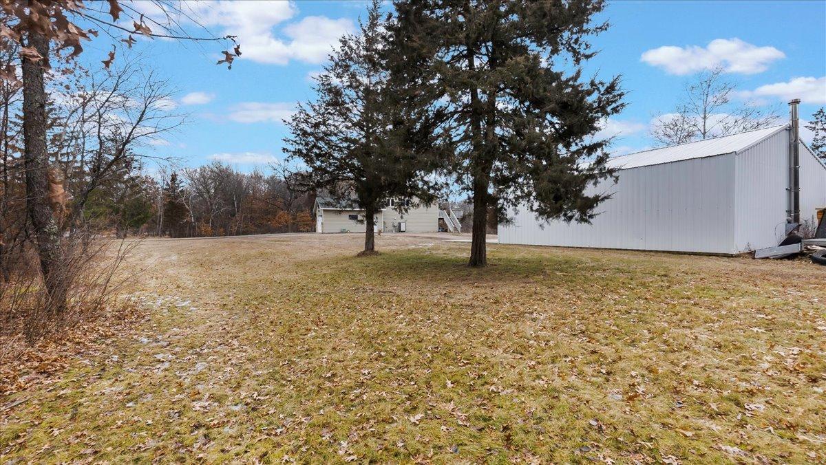 Yard with a large white metal outbuilding, a smaller building, and two evergreen trees.