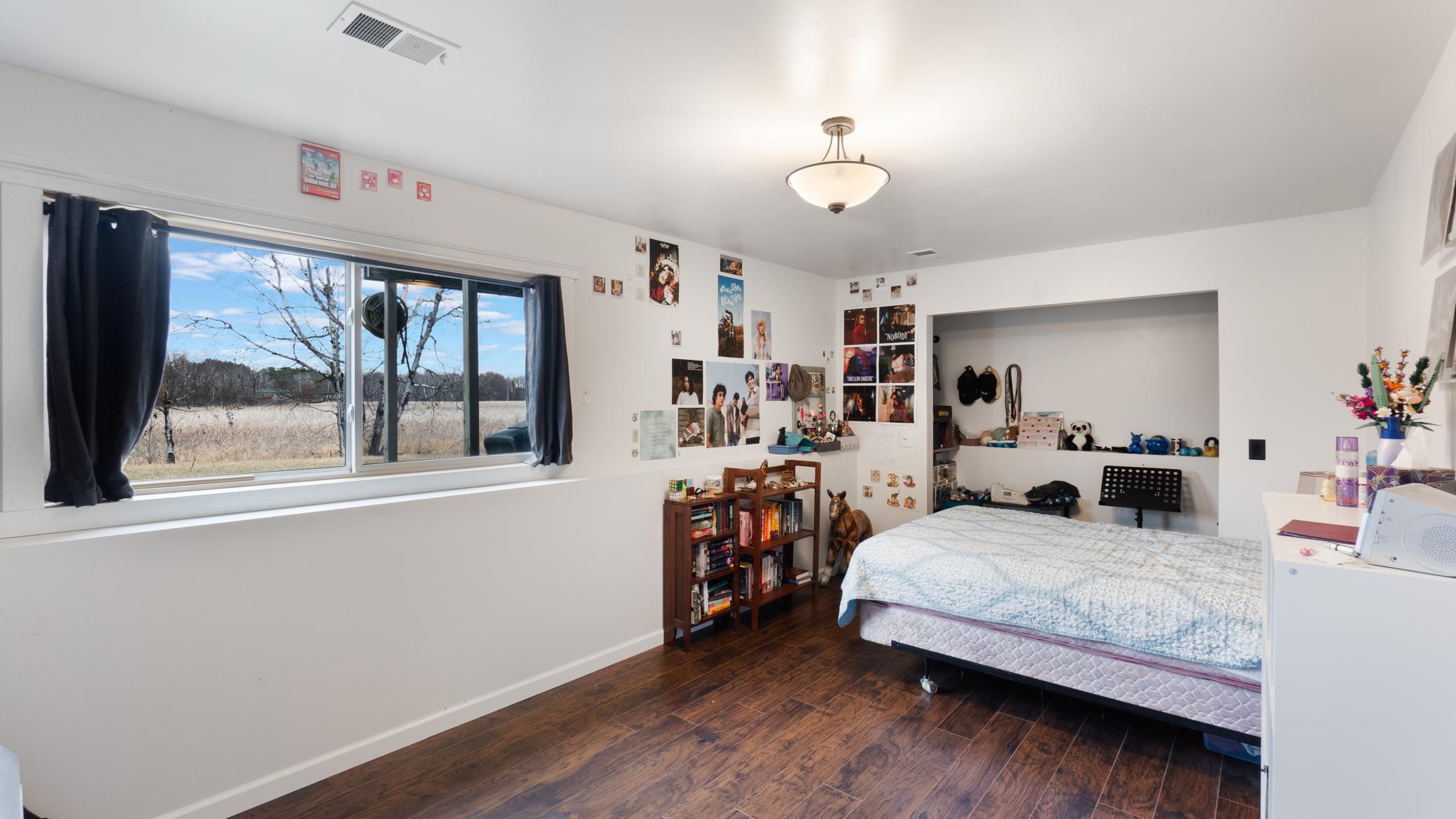 Bedroom with a wide window overlooking an open field and leafless trees.