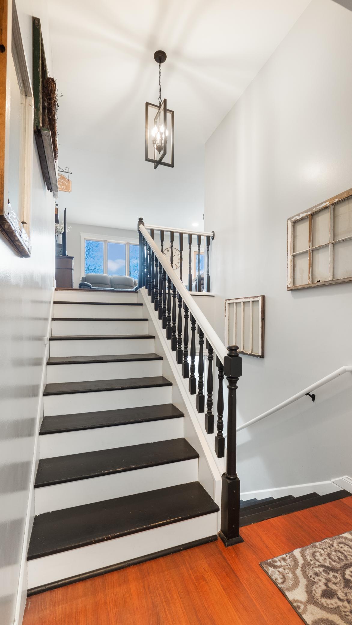 Entry staircase with dark treads and black railing, leading to a bright upstairs sitting area.