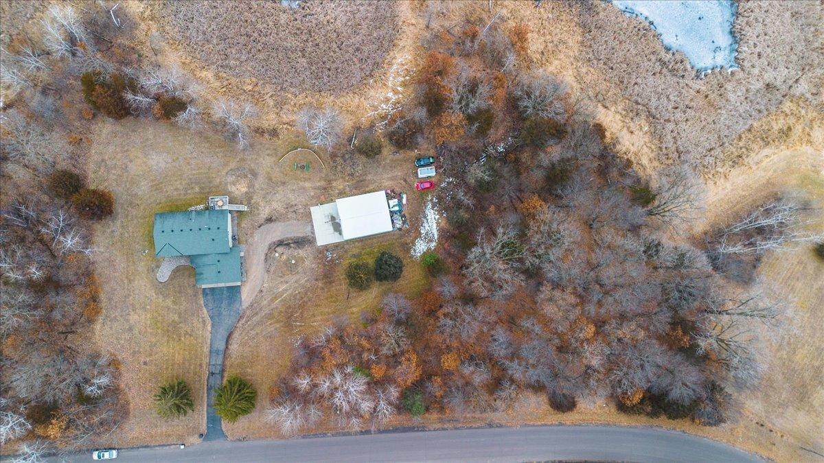 Aerial view of a wooded home property with a detached outbuilding, driveway, and nearby frozen water.