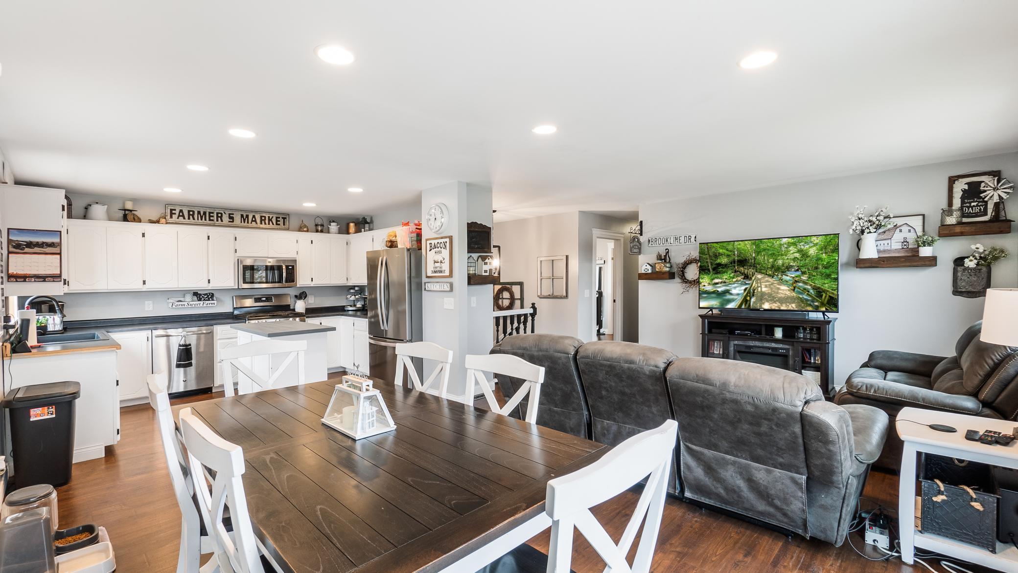 Open-plan kitchen and living room with white cabinets, stainless appliances, and a dark wood dining table.