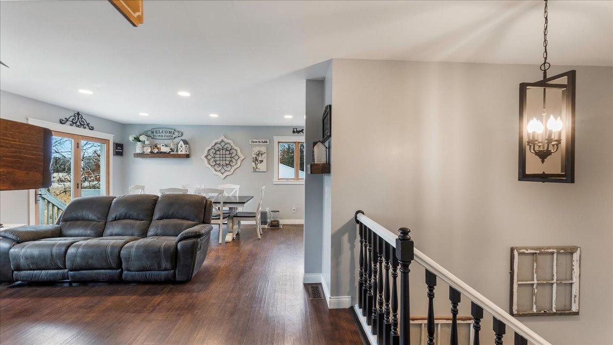 Living and dining area with a leather sofa, dark wood floors, and staircase with black railing.