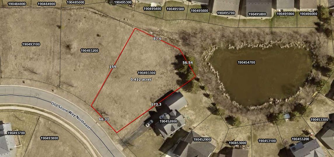 Aerial view of a grassy 0.412-acre lot outlined in red beside a pond and Old Stone Way Northeast.