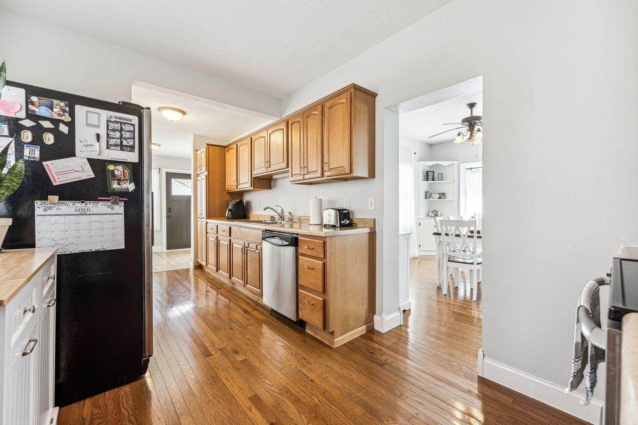 Kitchen with warm wood cabinets, a black refrigerator, stainless steel dishwasher, and hardwood floors.