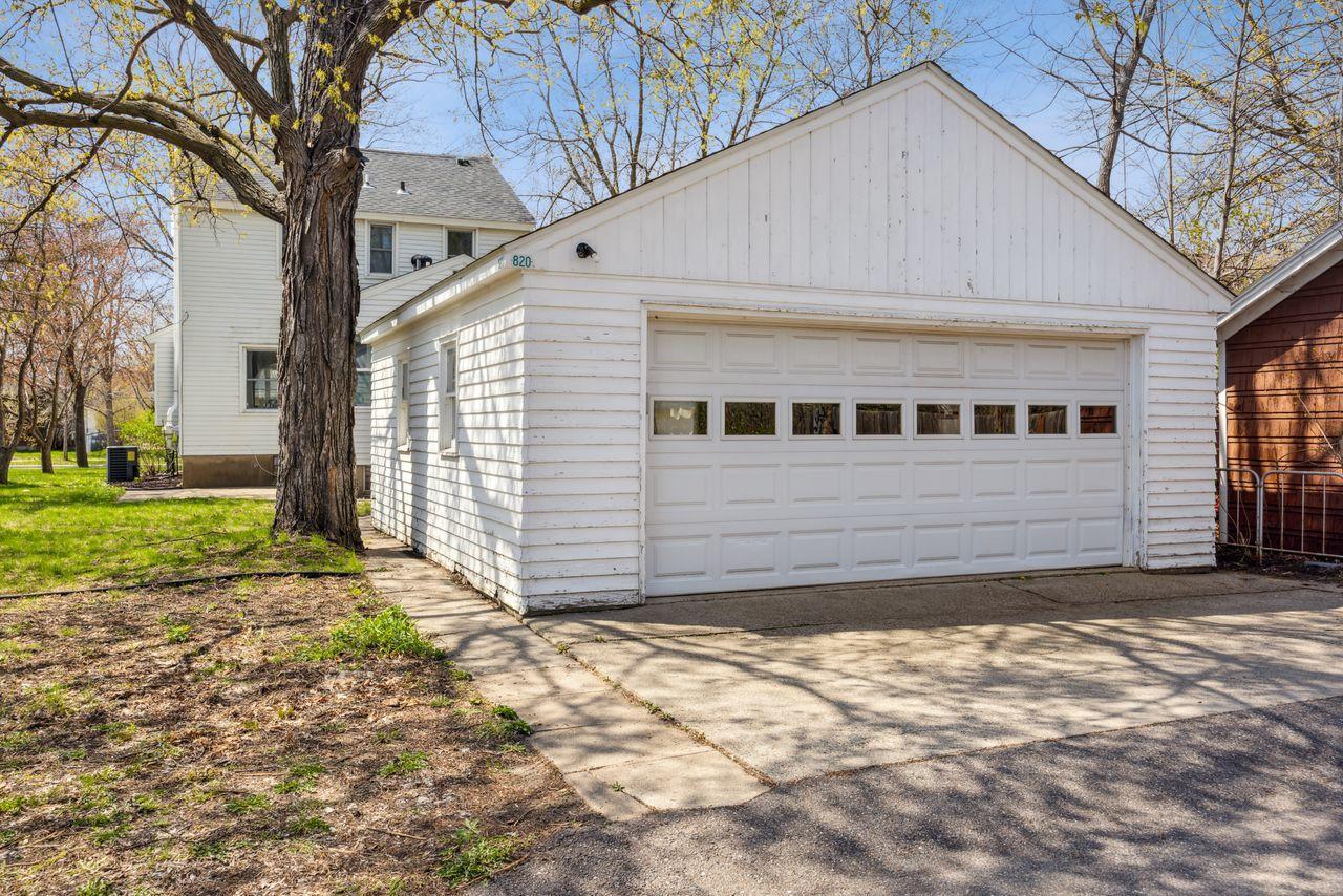 White detached garage with a wide paneled door and small windows, beside a mature tree.