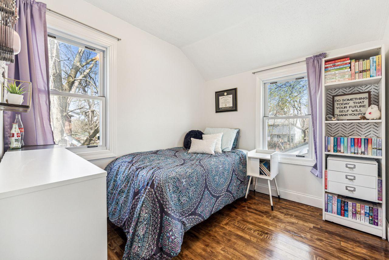 Bedroom with a blue patterned bedspread, purple curtains, and a bookcase filled with books.
