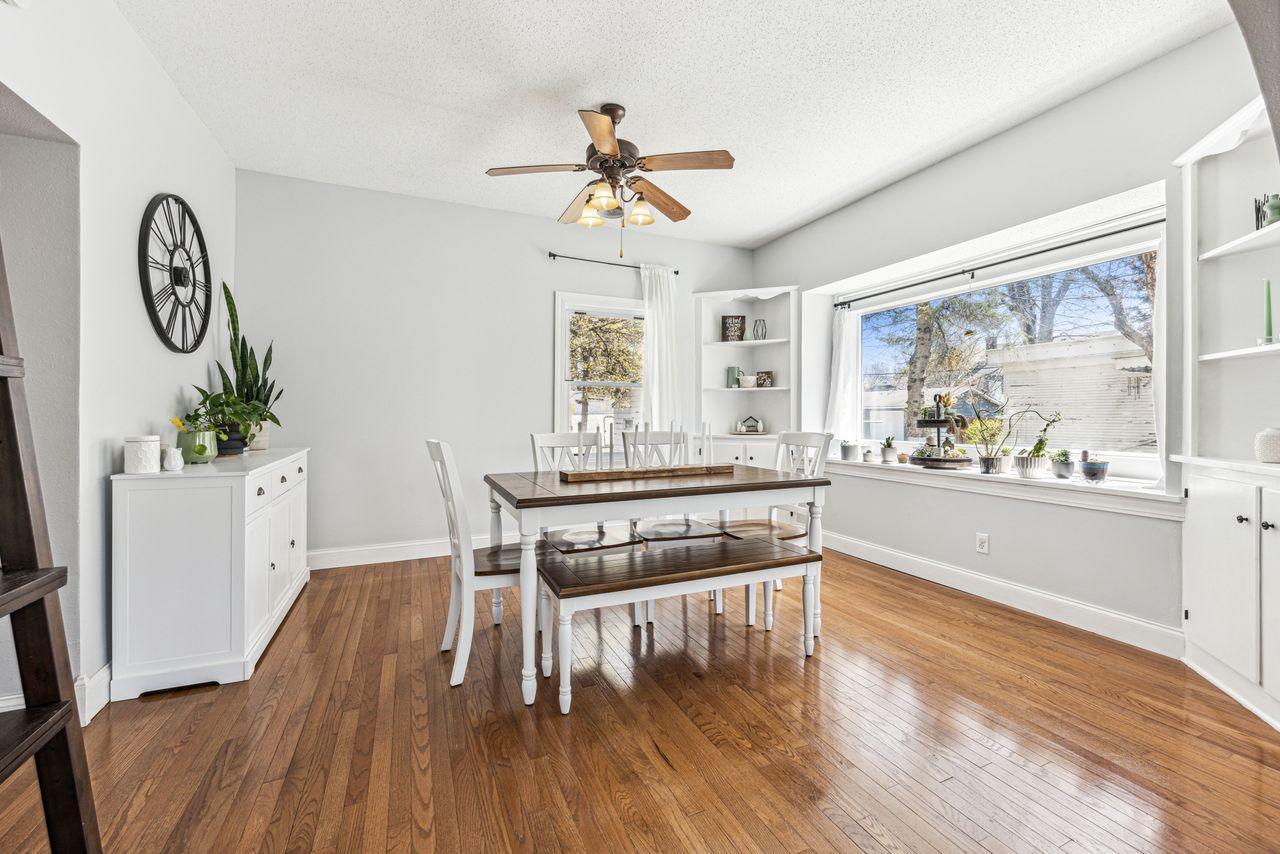 Dining room with warm hardwood floors, a white table and chairs, built-in shelves, and large windows.