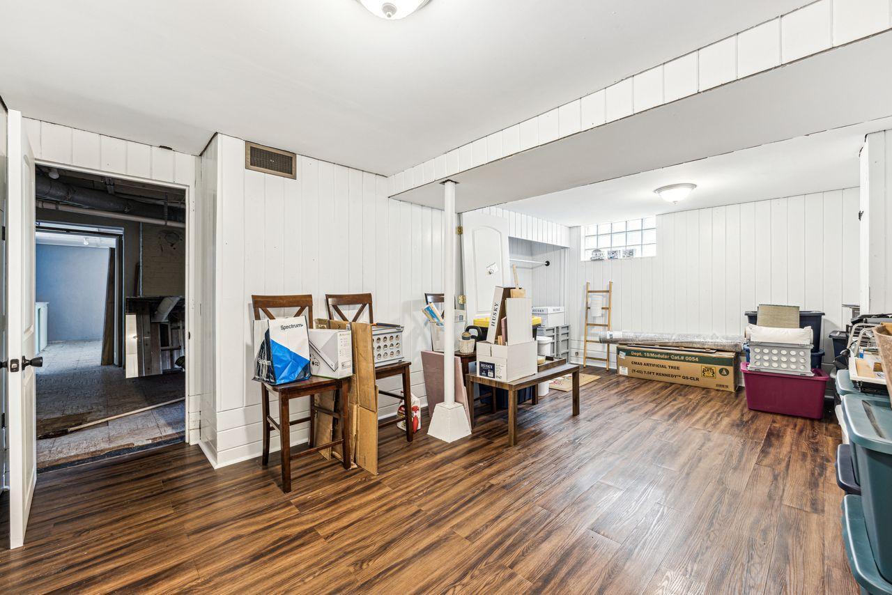 Large paneled room with wood-look flooring, a central support post, and stored boxes and furniture.
