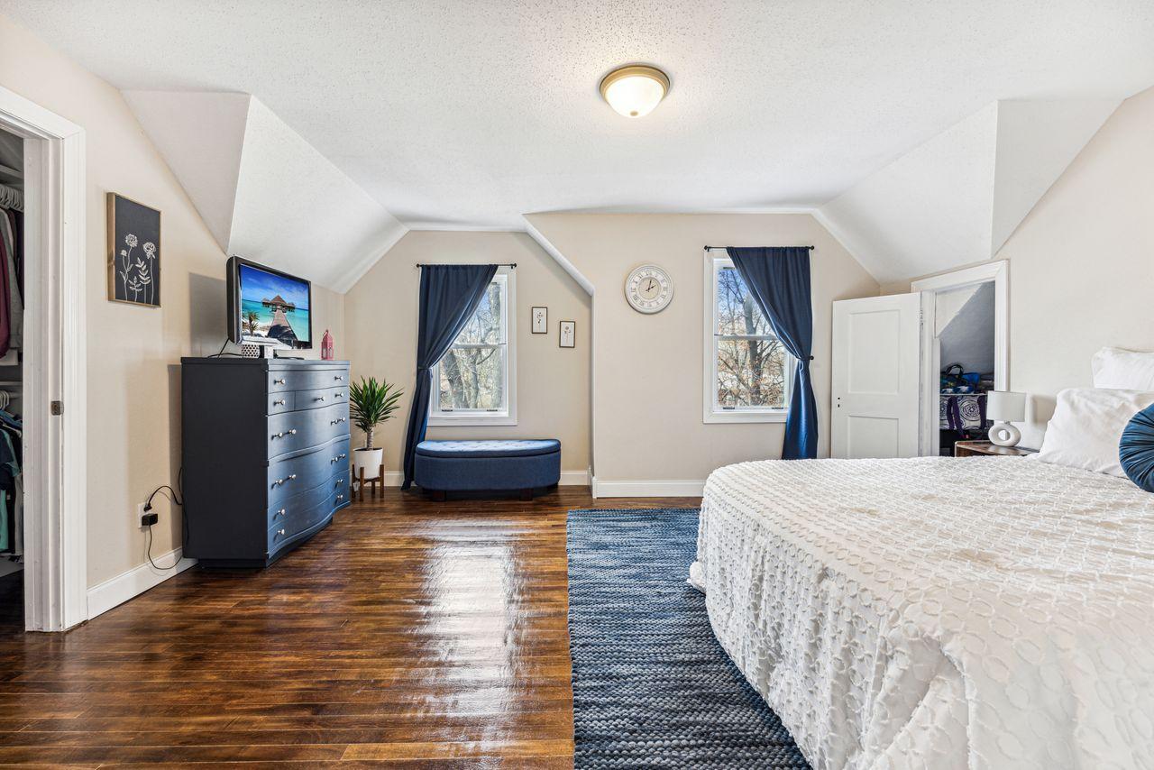 Bedroom with a white quilted bed, blue rug, dark wood floors, and sloped ceiling.