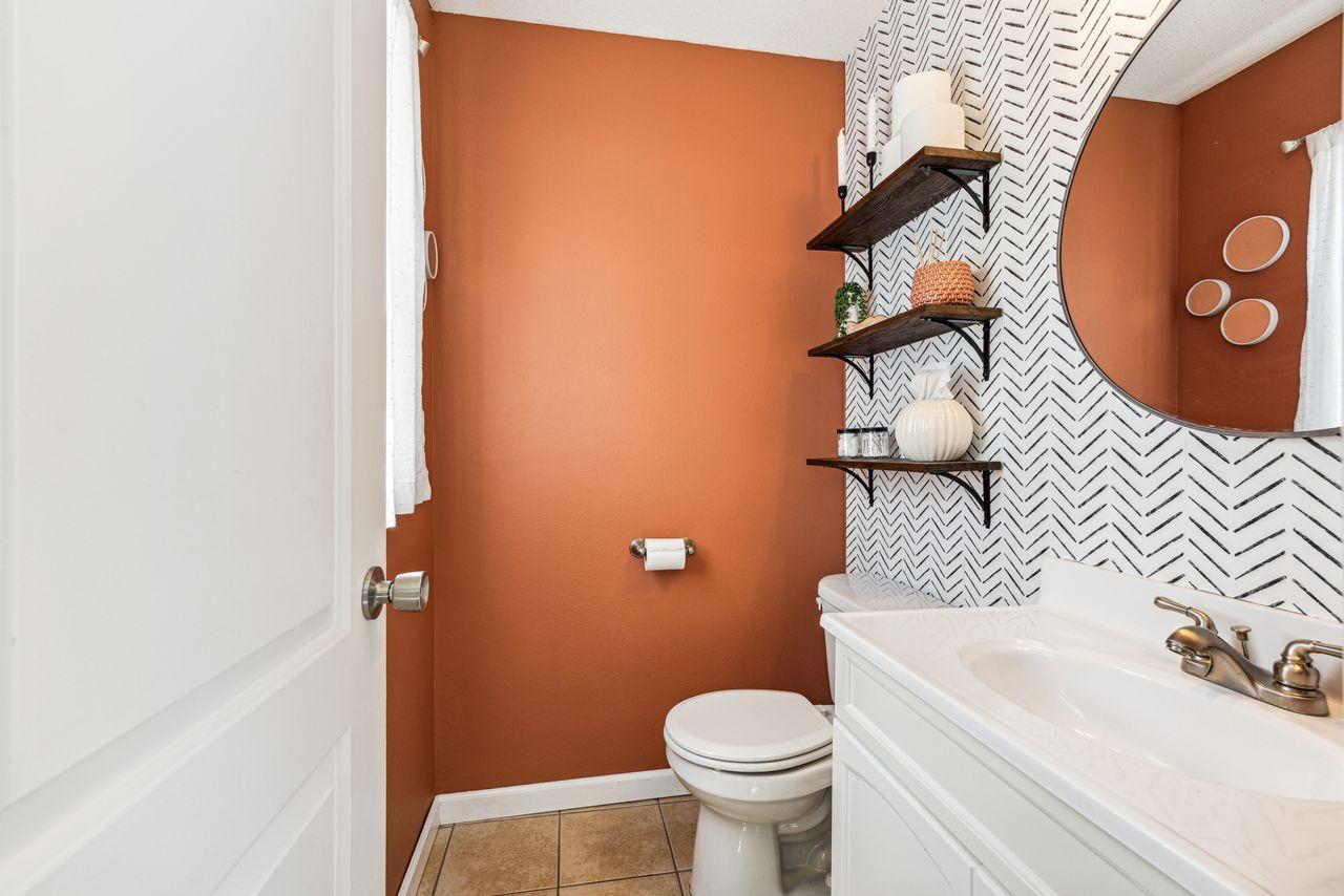 Bathroom with terracotta walls, patterned accent wall, white vanity, and large round mirror.