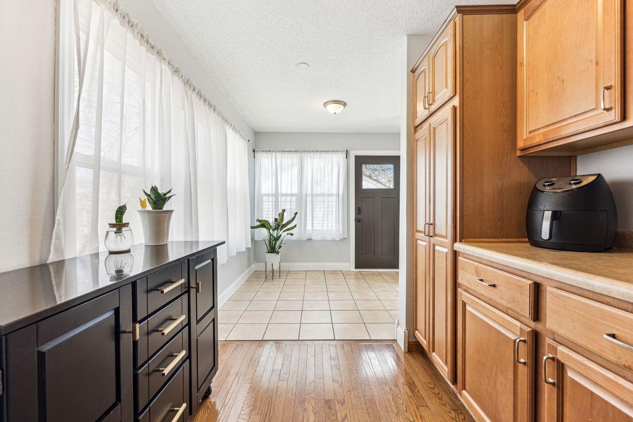 Kitchen with light wood cabinets, dark island, and a gray entry door beyond the tiled floor.
