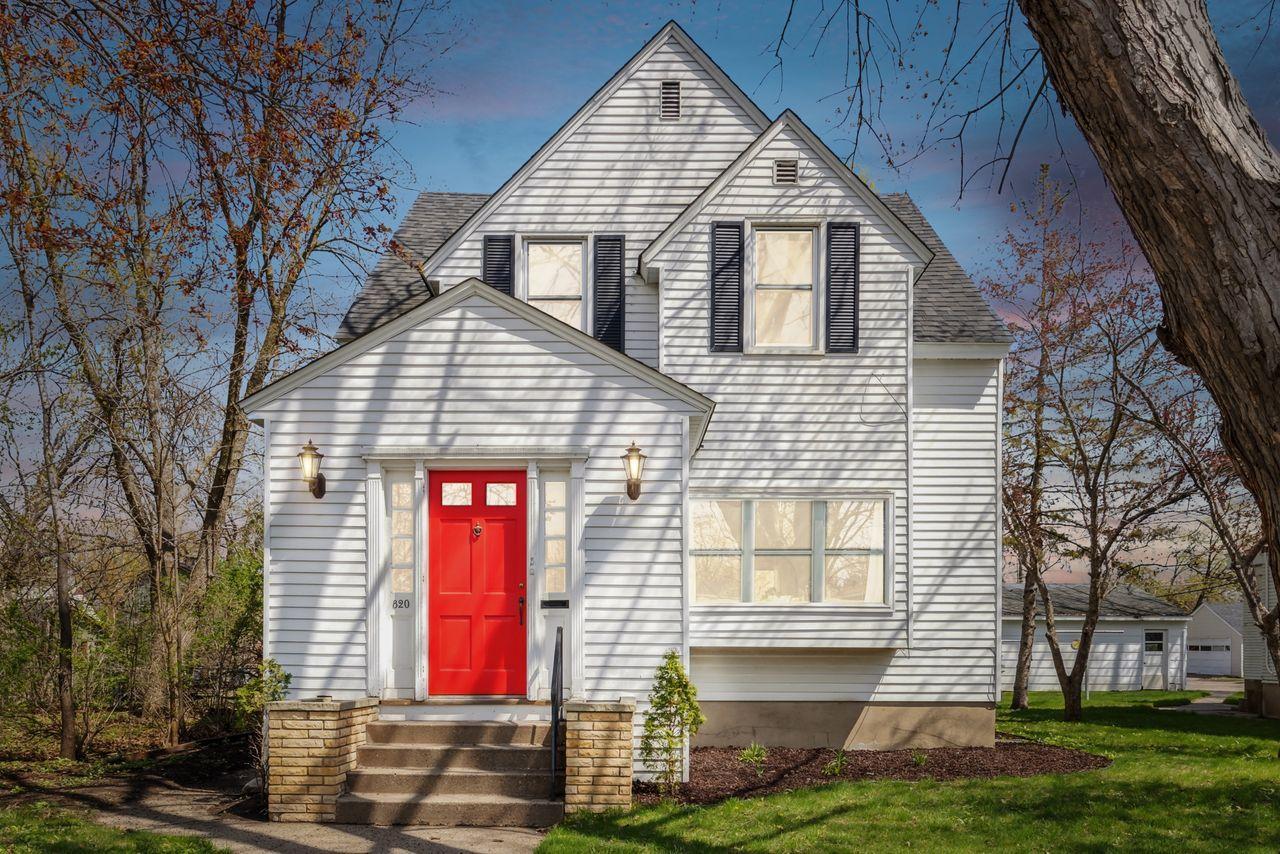 White two-story house with steep gables, dark shutters, and a bright red front door.