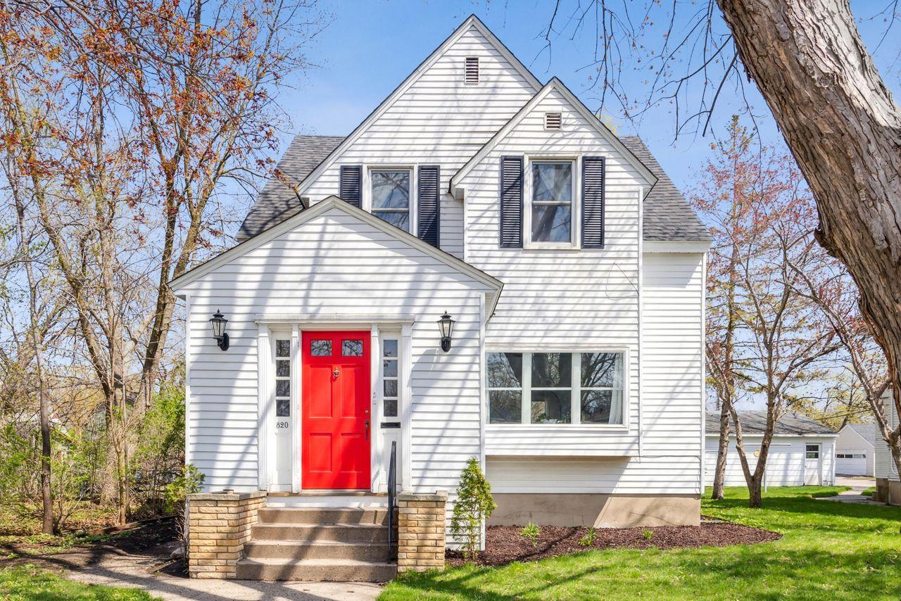 White two-story house with a bright red front door, black shutters, and a steep gabled roof.