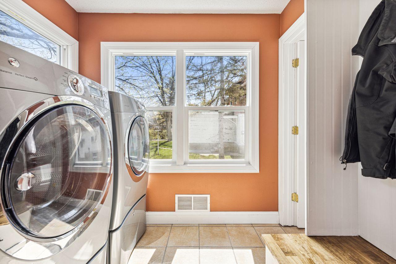 Laundry room with front-loading washer and dryer beneath a large window.