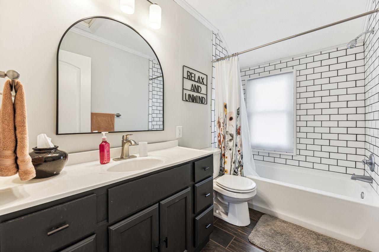 Bathroom with a dark vanity, arched mirror, and white subway-tile tub surround.