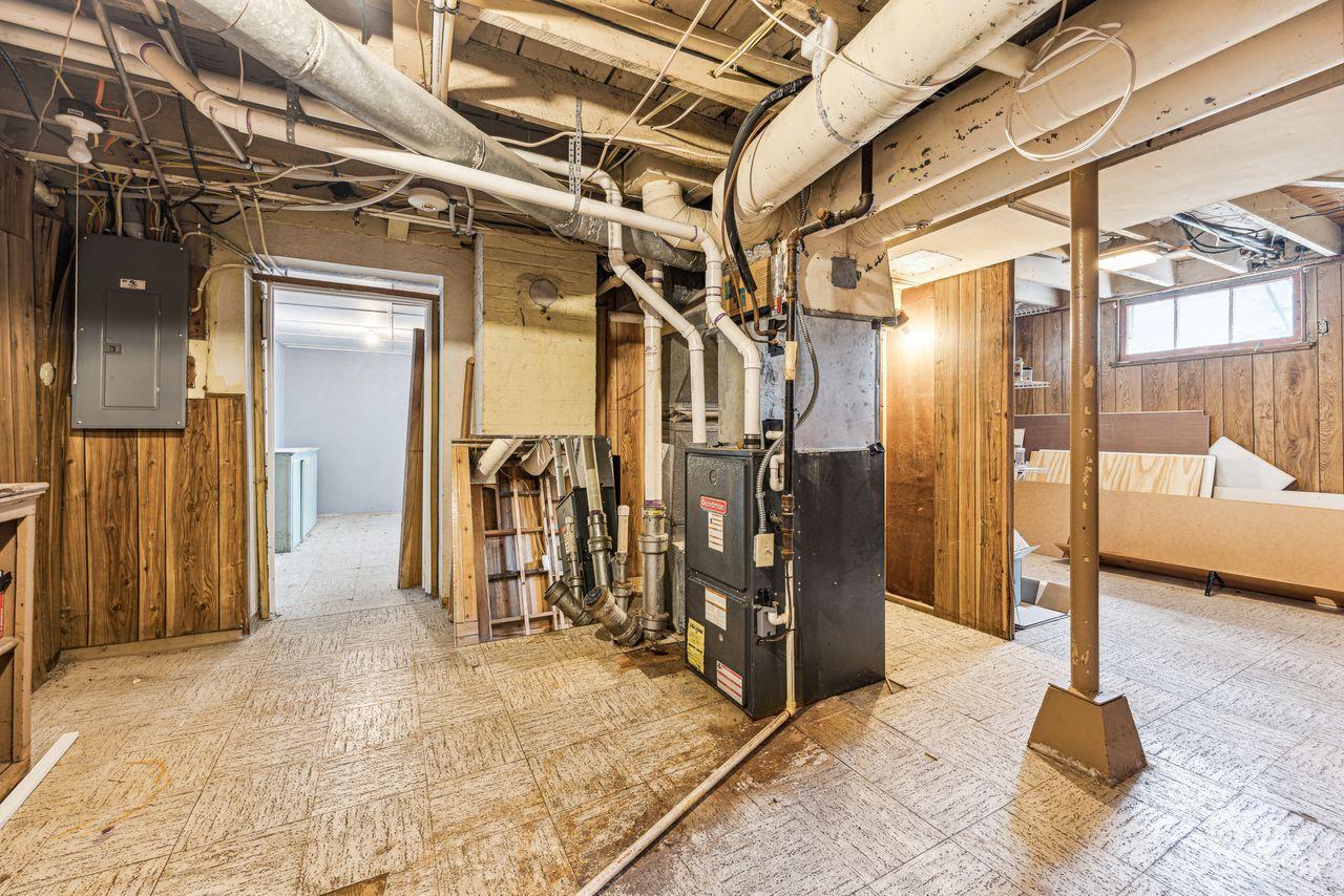 Unfinished basement utility area with a furnace, exposed ductwork, and wood-paneled walls.