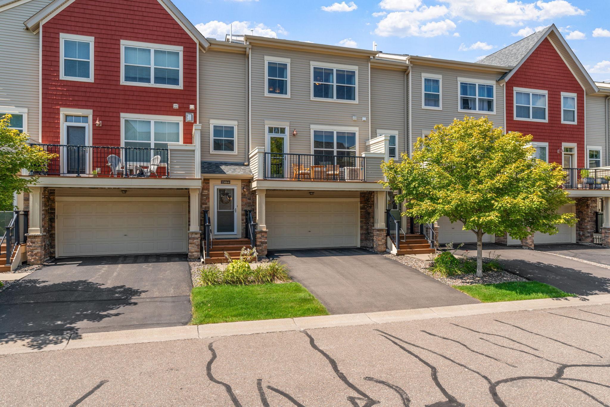 Townhouse exterior with attached garages, raised decks, and a leafy tree beside the driveway.