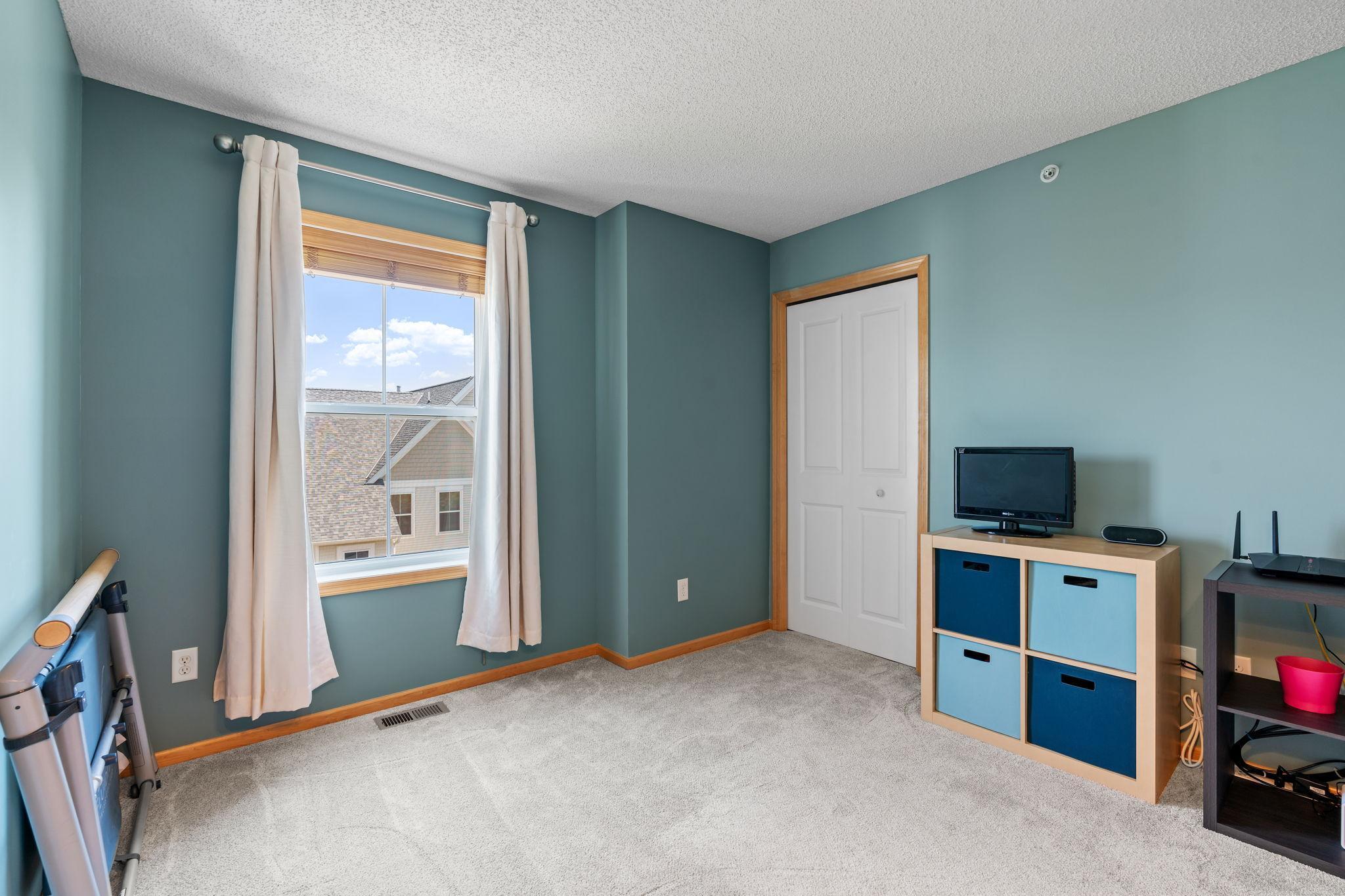 Bedroom with teal walls, gray carpet, a curtained window, and a television on a storage unit.