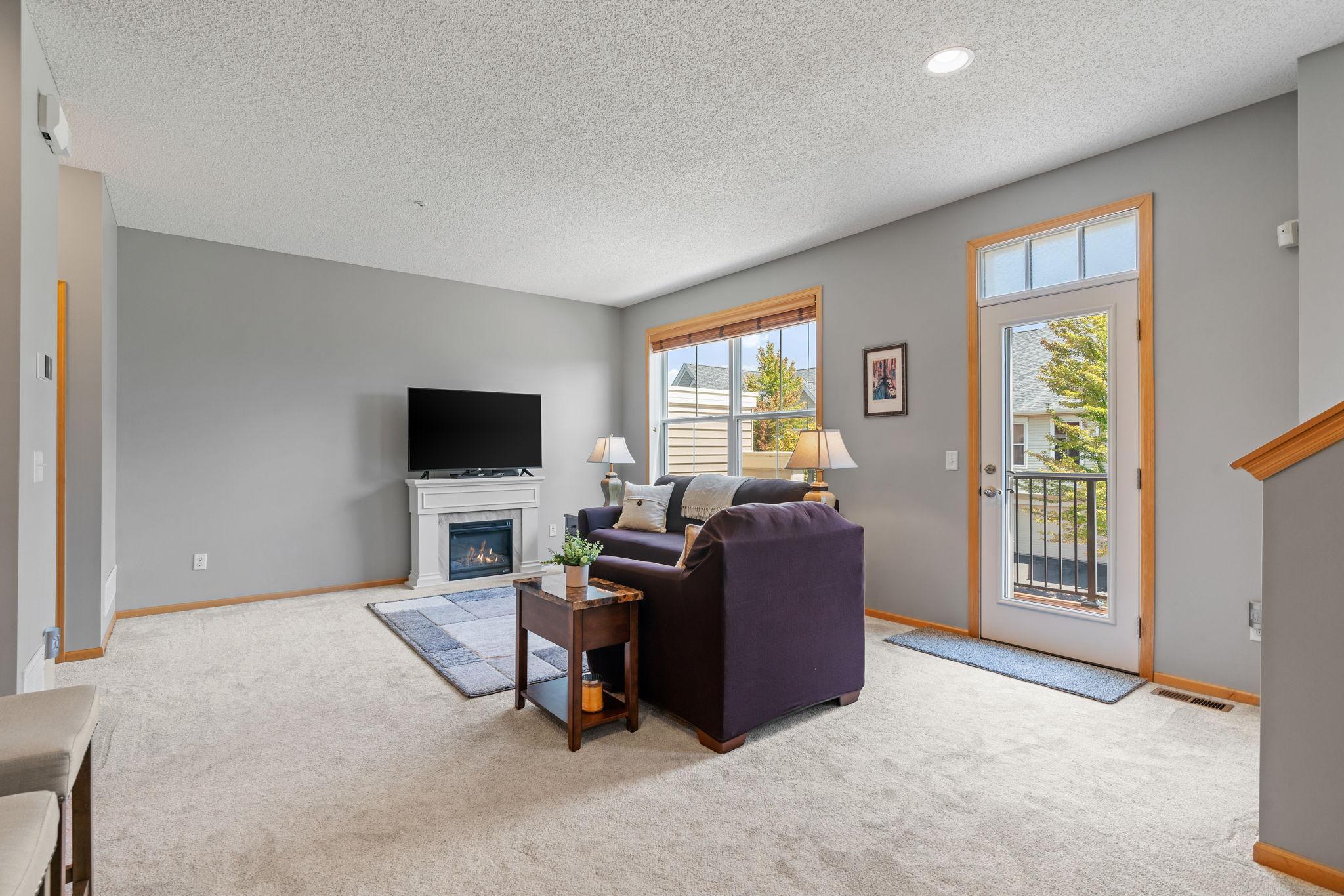 Furnished living room with a dark sectional, gas fireplace, and glass balcony door.