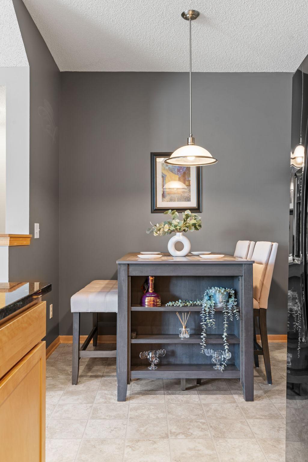 Dining area with a gray serving table, upholstered chairs, and a pendant light.