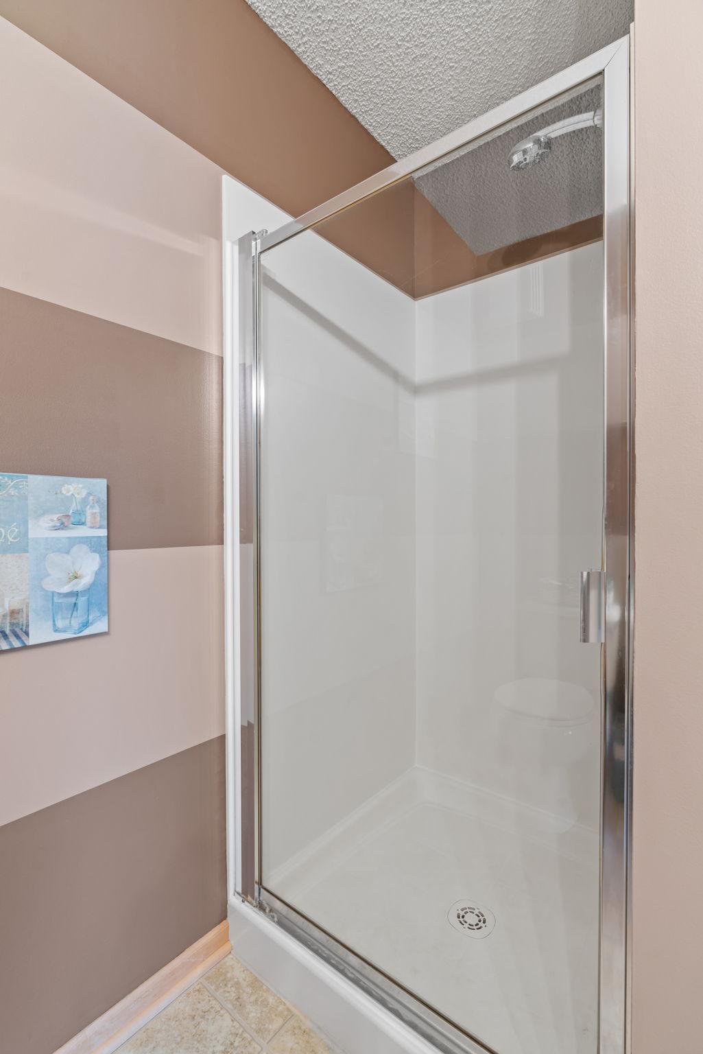 Bathroom shower with a clear glass enclosure, chrome frame, and striped taupe and pale pink walls.