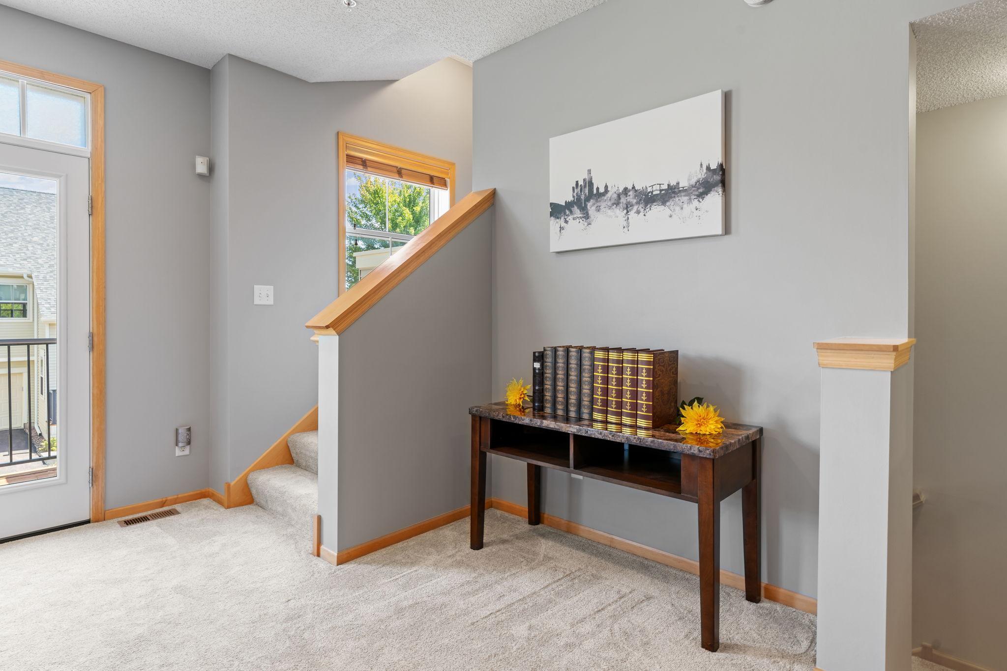 Furnished entryway with a carpeted staircase and console table decorated with books and yellow flowers.