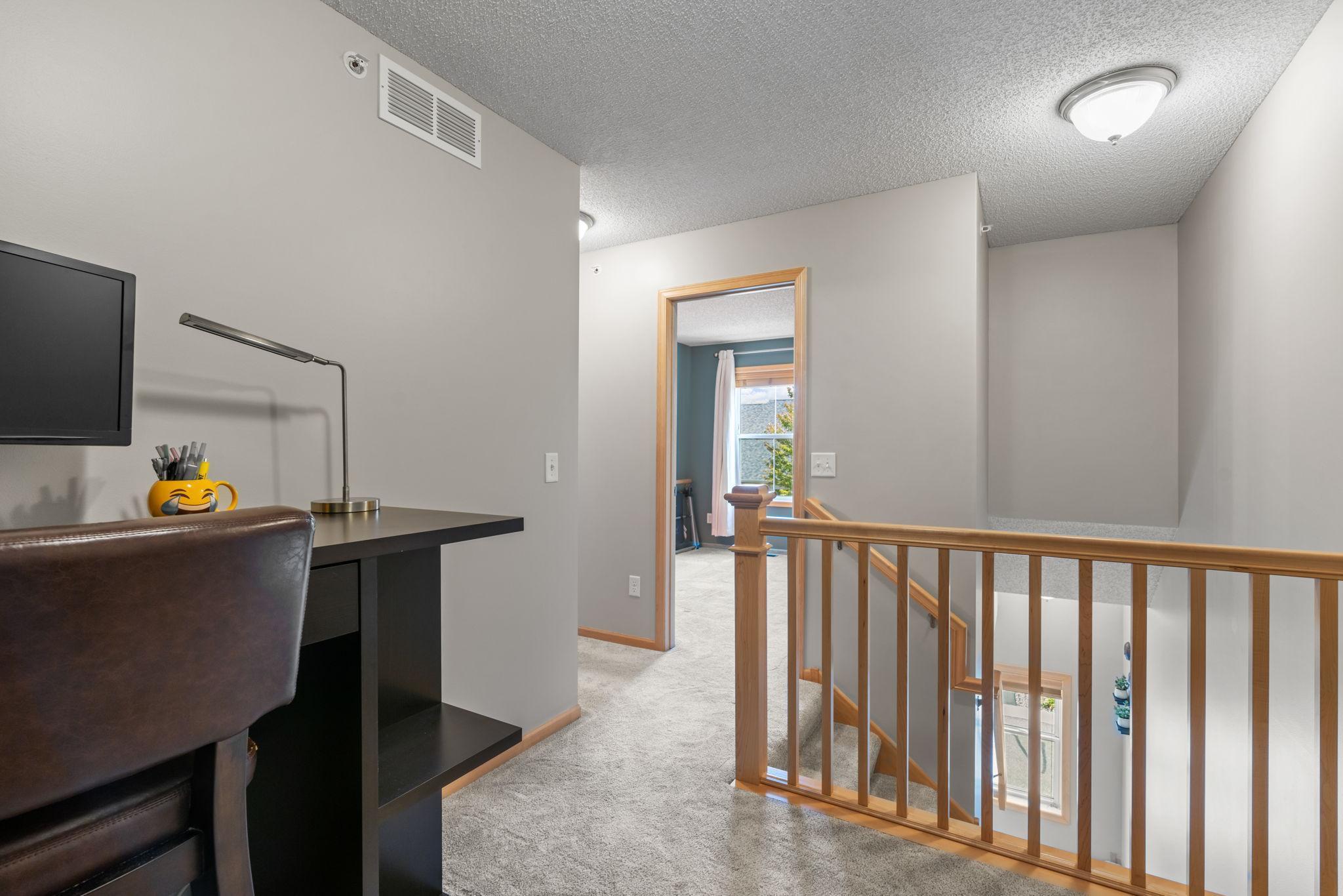Upstairs landing with a desk beside a wooden stair railing overlooking the staircase.