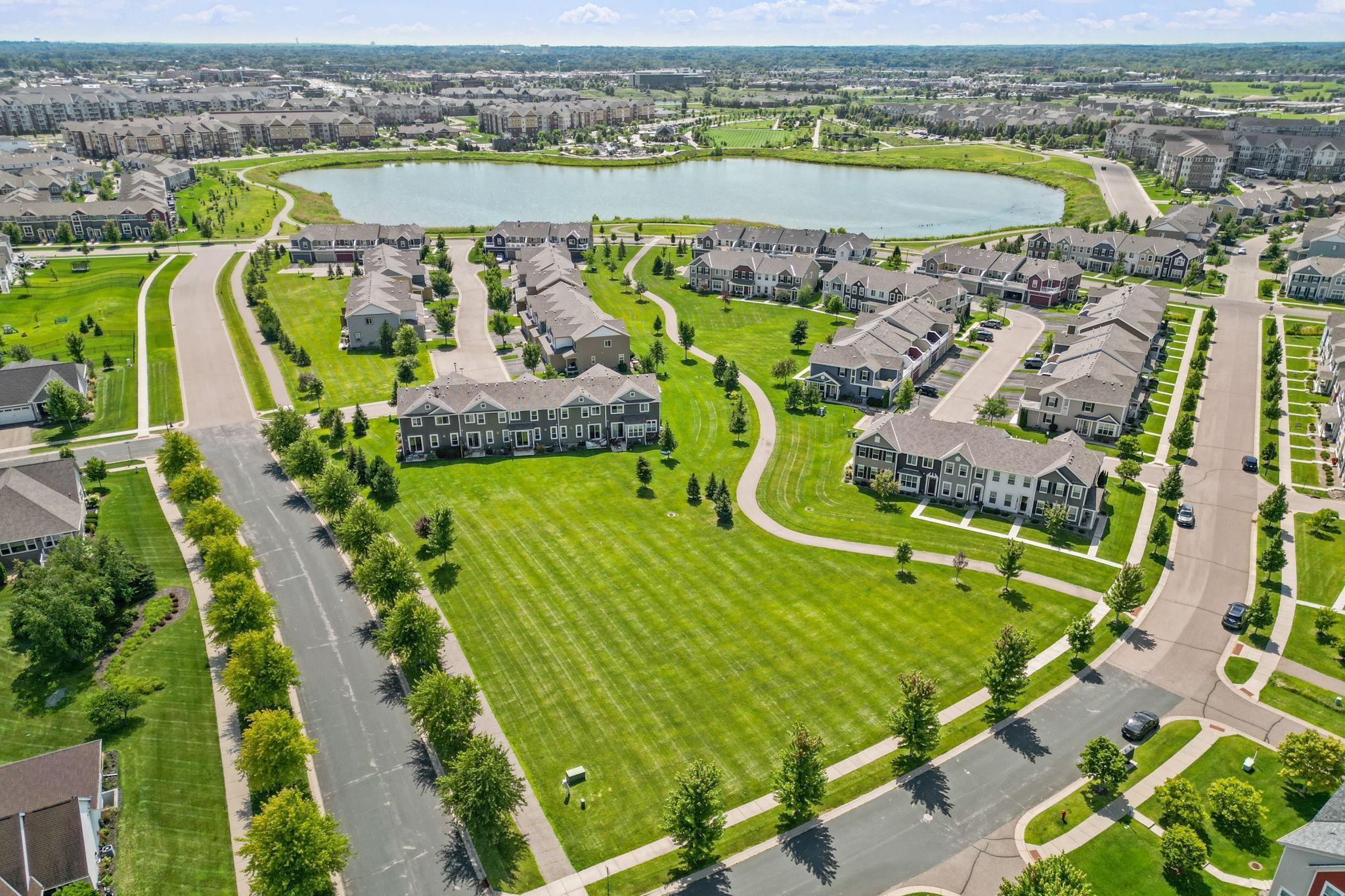 Aerial view of townhomes around a pond, with broad lawns and curving walking paths.