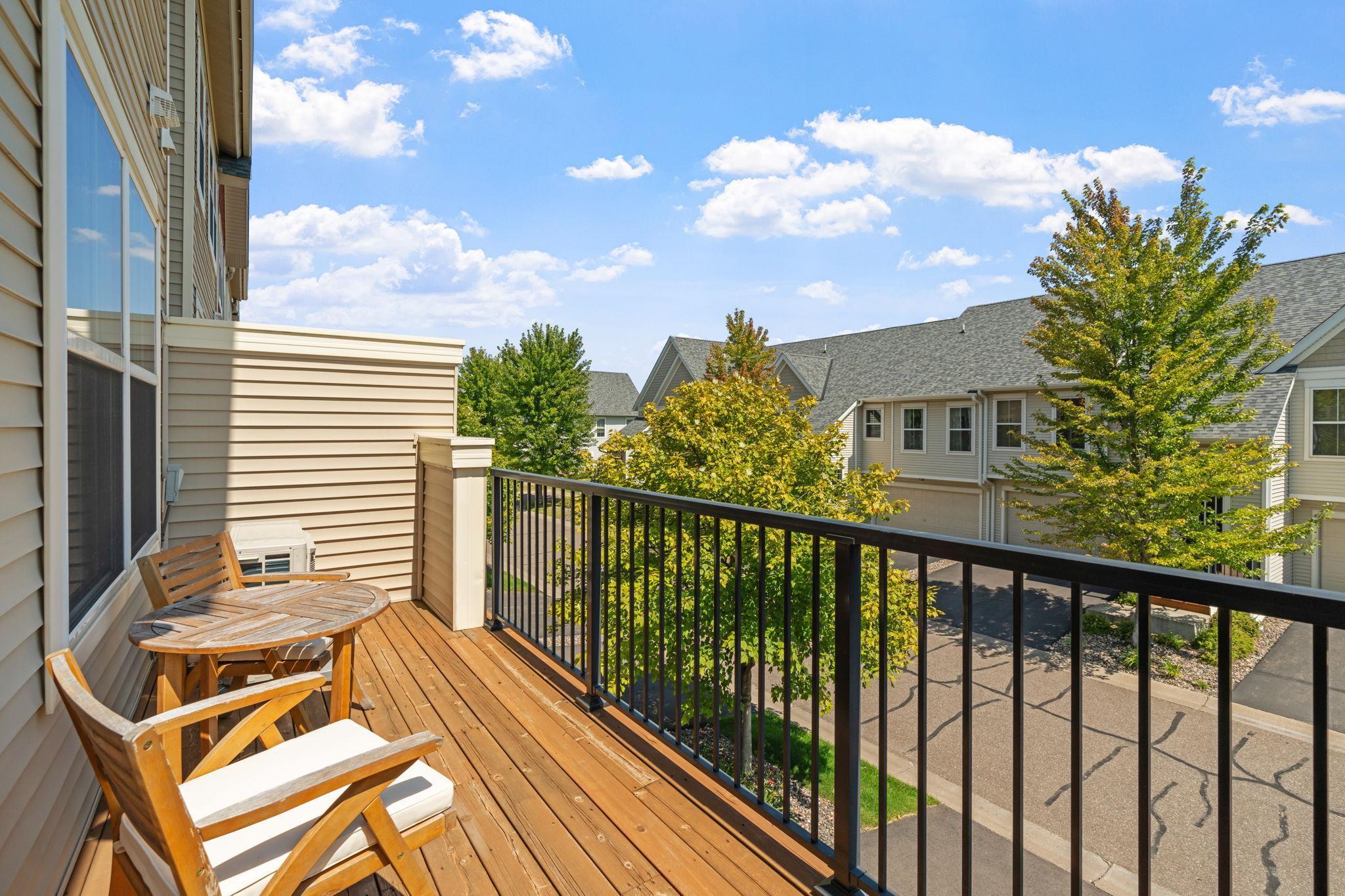 Wooden balcony deck with patio chairs and table overlooking trees and neighboring townhomes.