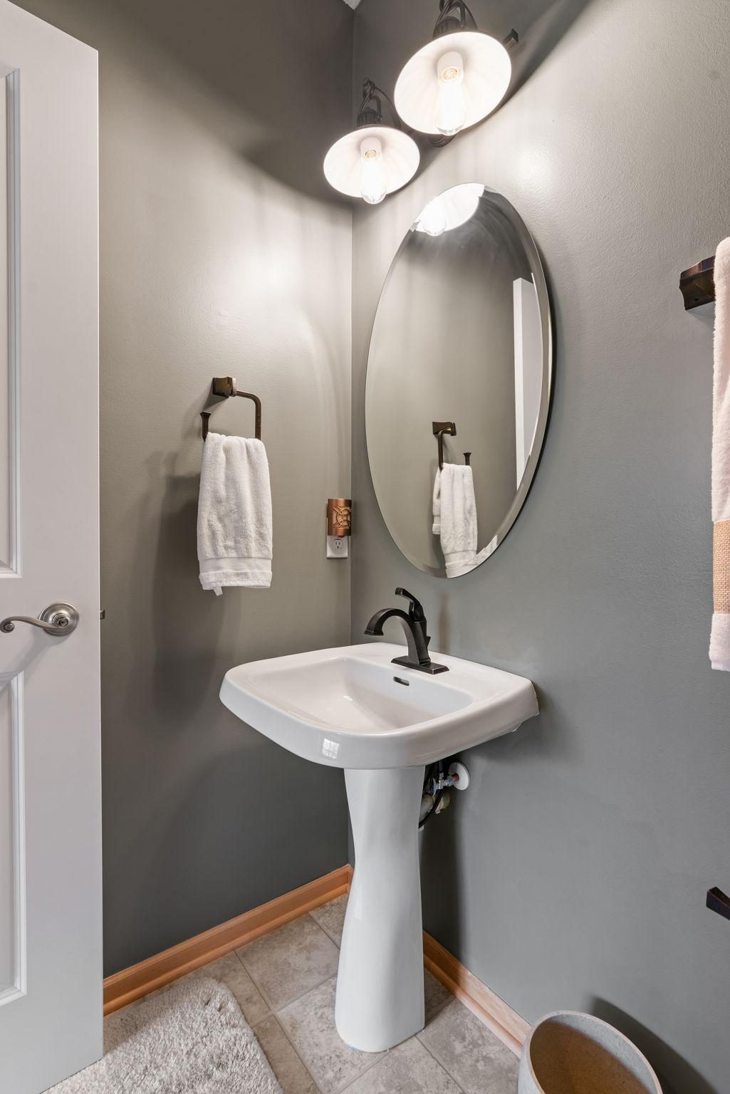 Bathroom with a white pedestal sink, black faucet, and large oval mirror.