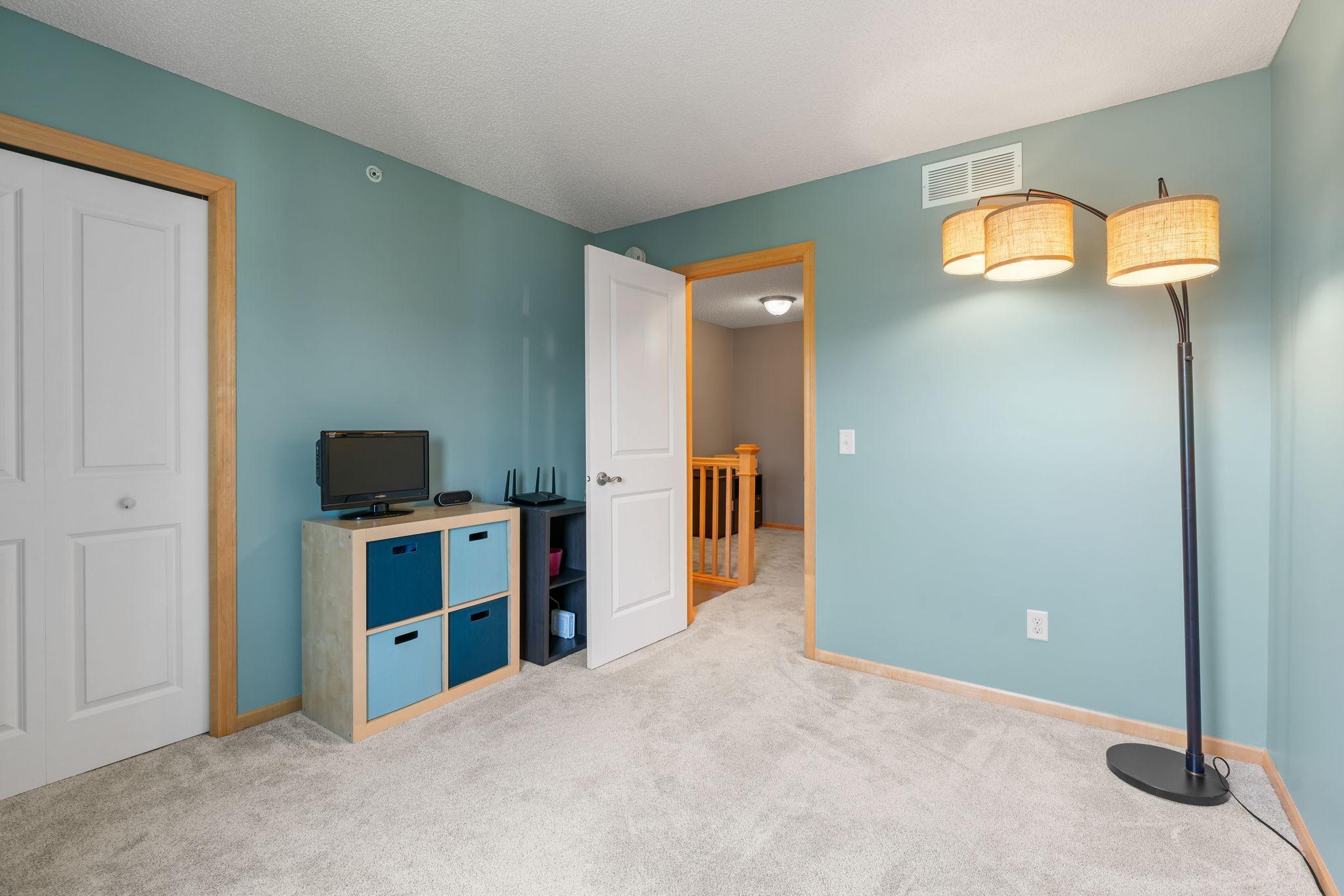 Carpeted room with teal walls, a TV on cube storage, and a lit floor lamp beside an open doorway.