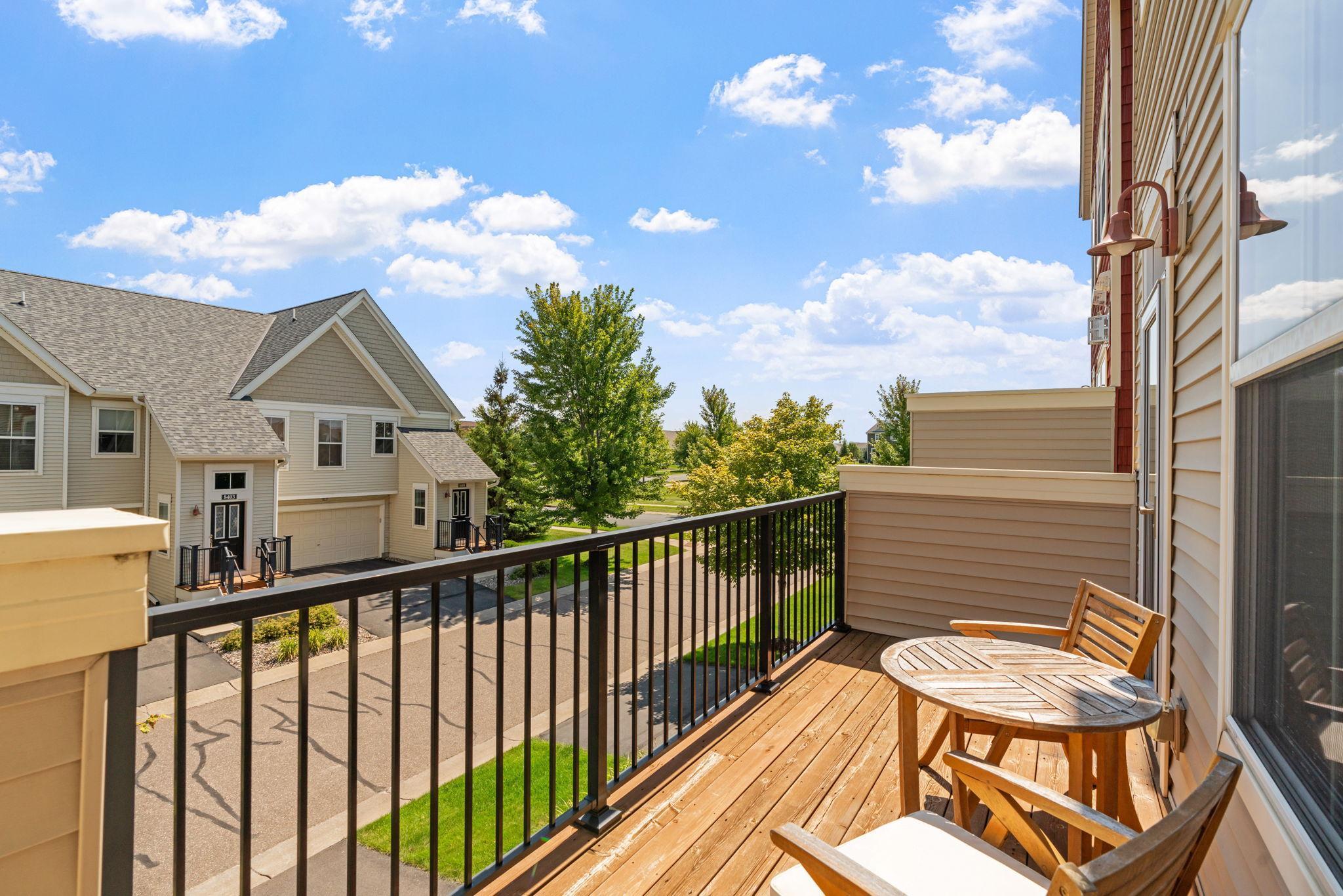 Condo balcony with wooden decking, a round table and chairs, overlooking neighboring homes and trees.